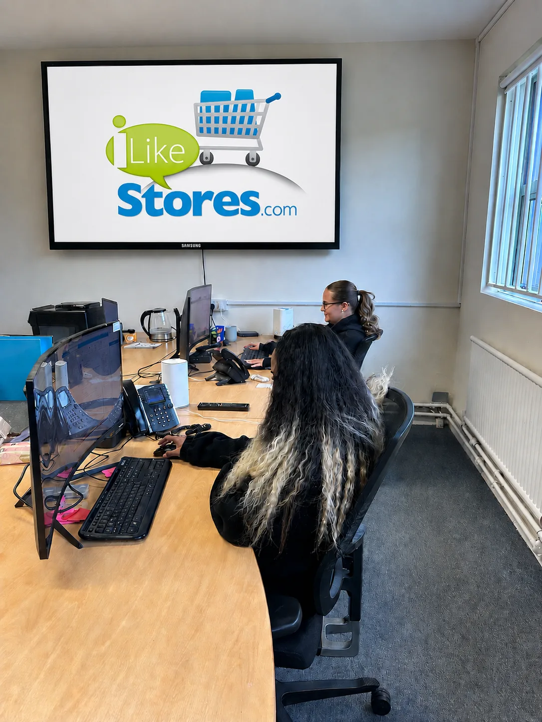 Office team working at desks with iLikeStores logo on wall screen